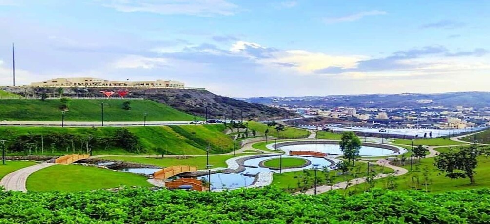 A landscaped park with winding paths, a bridge, and a distant hilltop building. 1