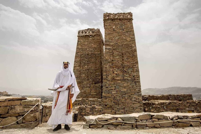 A person standing in front of ancient stone towers with intricate carvings, in a historical site with a clear sky. 2