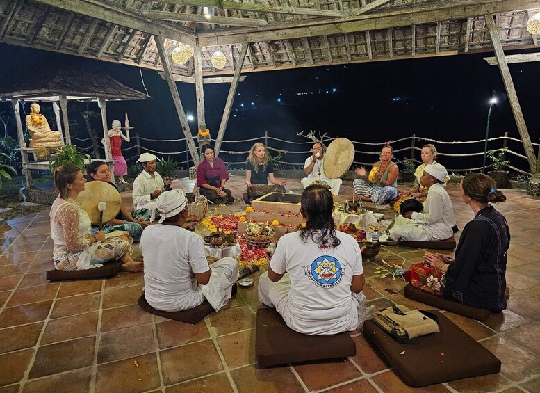 A group of people sitting in a circle on the ground, engaged in a ritual with flowers and traditional instruments. 1