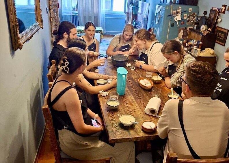 A group of people sitting around a wooden table, engaged in a meal with bowls, plates, and a blue water bottle. 5
