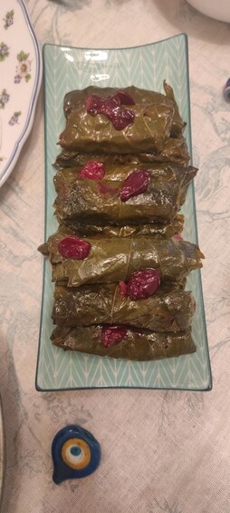 A plate of stuffed grape leaves with red pepper pieces on a patterned tablecloth. 2