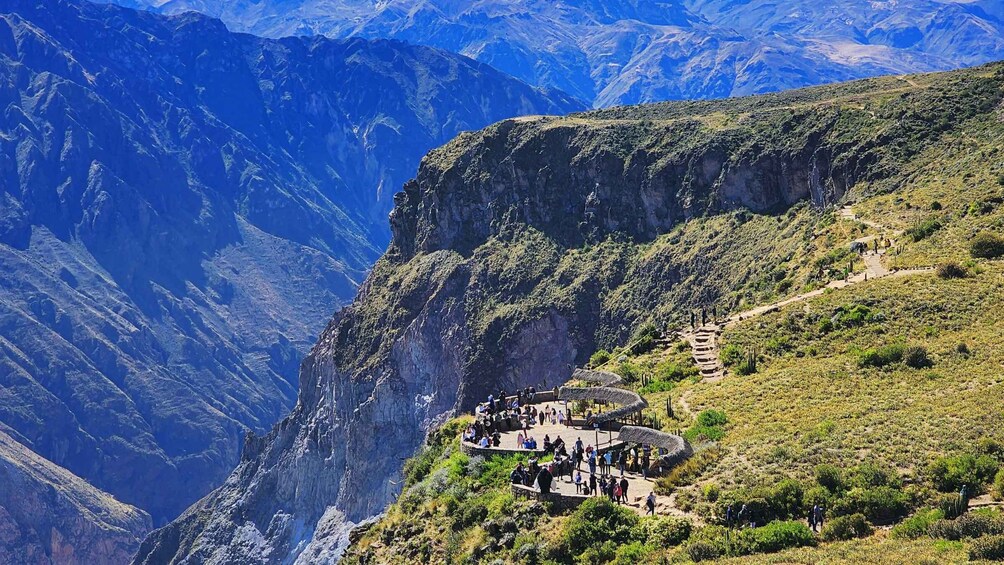 A mountainous landscape with a group of people gathered around a thatched-roof structure on a hillside. 4