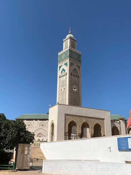 A tall minaret with intricate tile work, a mosque with arches, and a clear blue sky. 1
