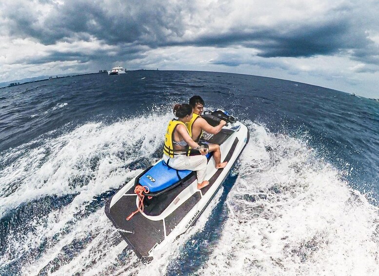 Two people jet-skiing on a body of water with a distant ship and cloudy sky. 2