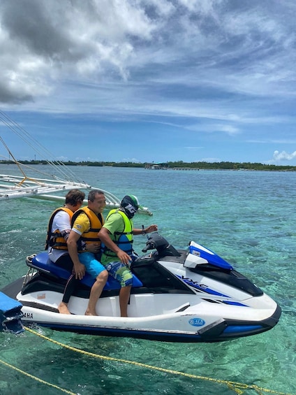 Three people on a jet ski in clear water with a distant shoreline. 3