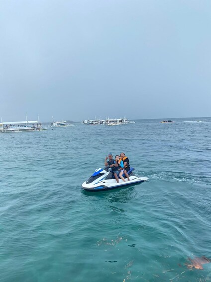 A jet ski with three people on it, water in the foreground, and boats in the background. 5
