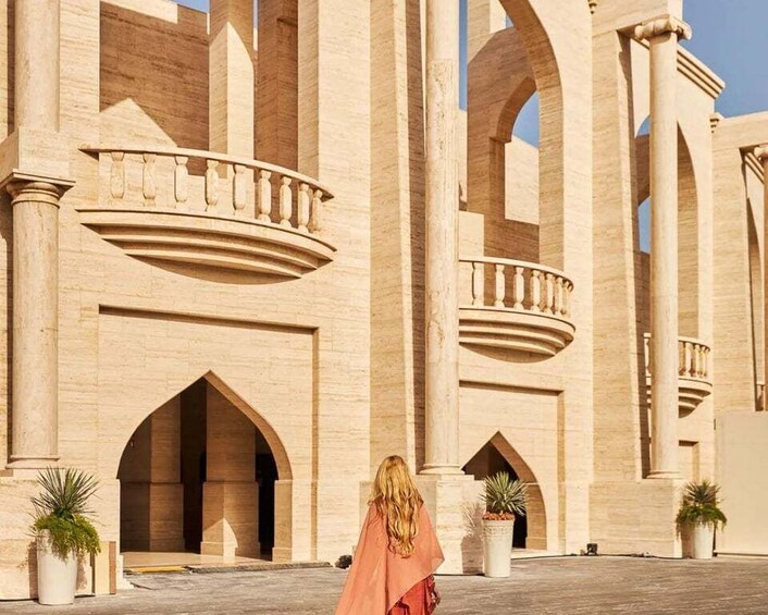 A person walking in front of a large, arched building with columns and balconies. 3