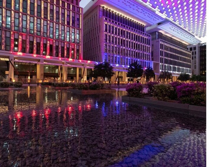 A modern building complex with illuminated windows and a reflective water feature in front. 5