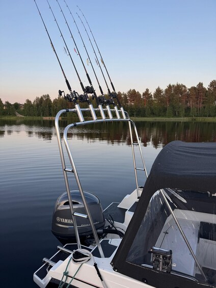 A boat with multiple fishing rods mounted on a metal rack, a Yamaha outboard motor, and calm water reflecting the surrounding trees. 1