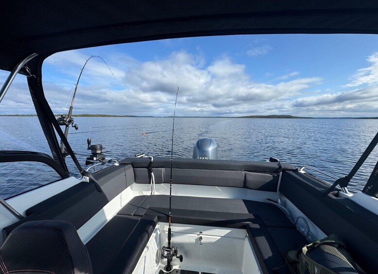 A boat's interior with fishing rods and a motor on the deck, facing a calm lake with distant land. 3