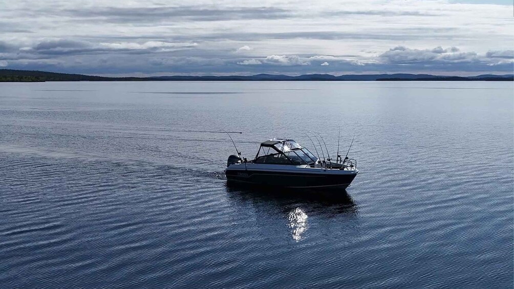 A boat on calm water with a cloudy sky and distant mountains. 1