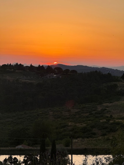A sunset over a hilly landscape with scattered trees and a small settlement. 5