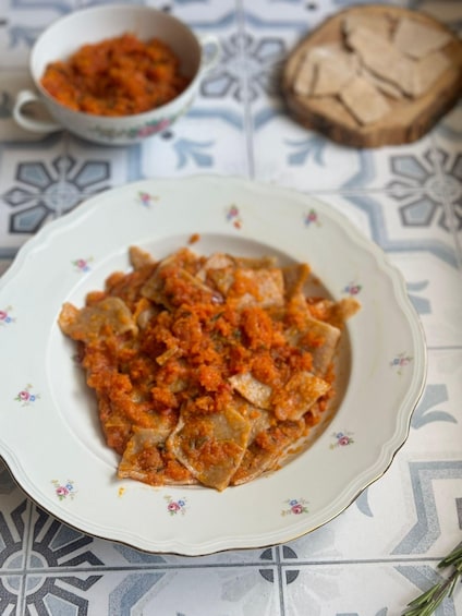 A plate of stuffed pasta with a tomato-based sauce, a bowl of sauce, and a loaf of bread on a patterned tablecloth. 2