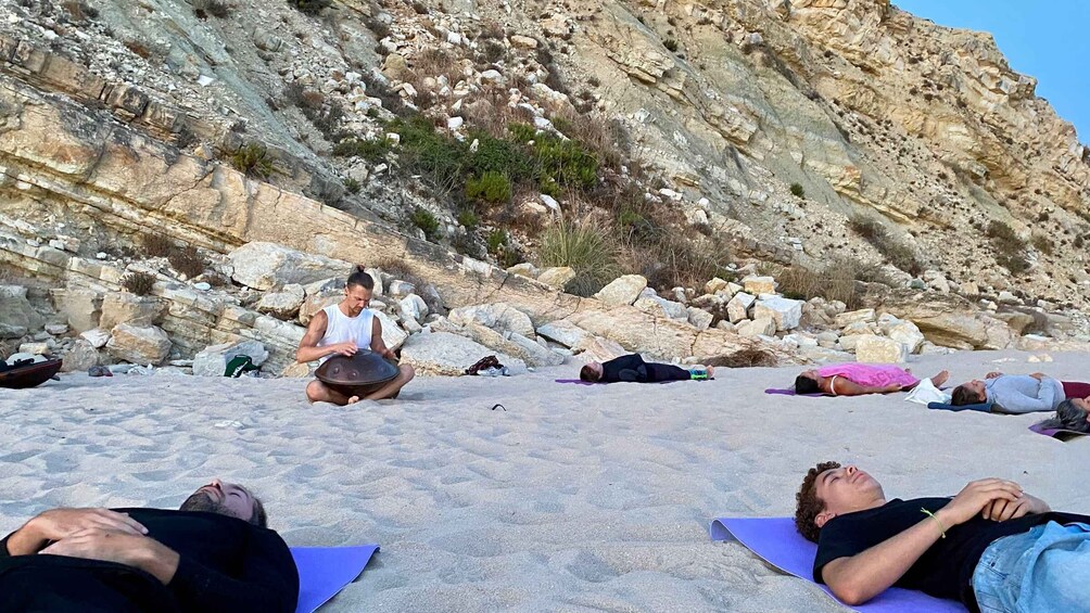 People meditating on a beach with rocky cliffs in the background. 5