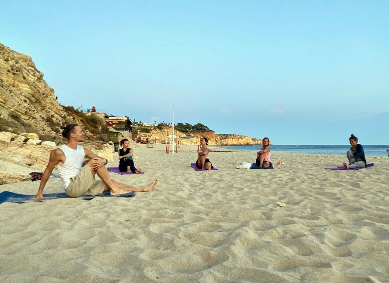A group of people practicing yoga on beach mats. 3