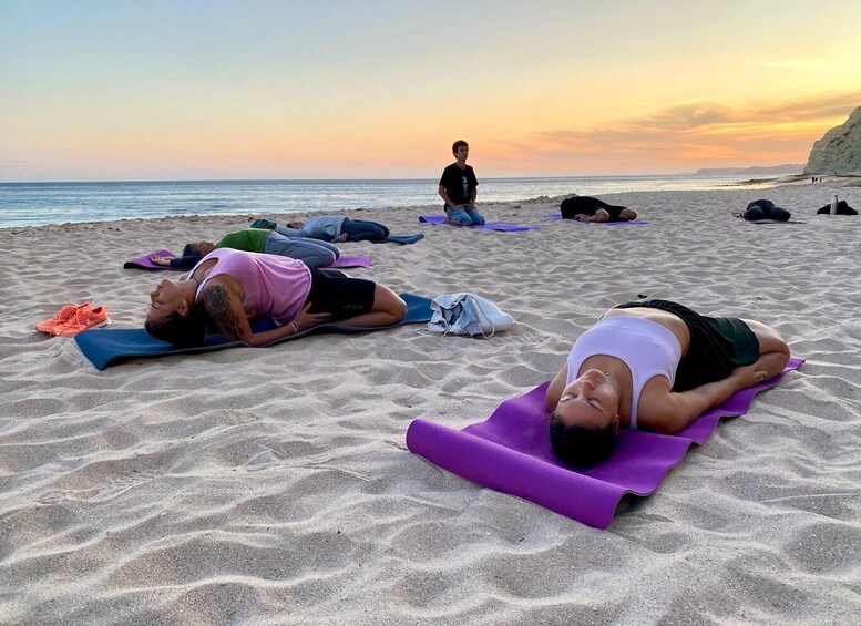 A group of people practicing yoga on mats on a beach at sunset. 5