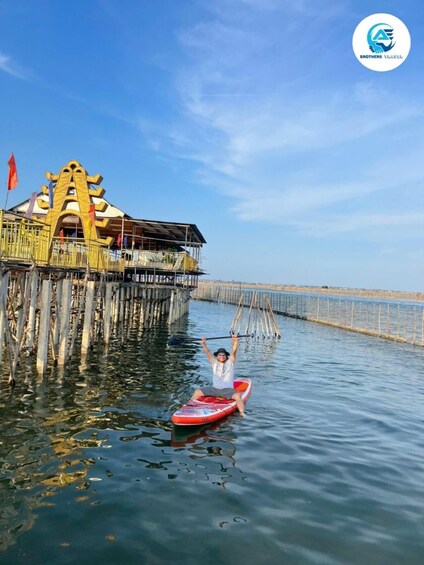 A person paddleboarding on calm water with a wooden pier and a distinctive yellow structure in the background. 4