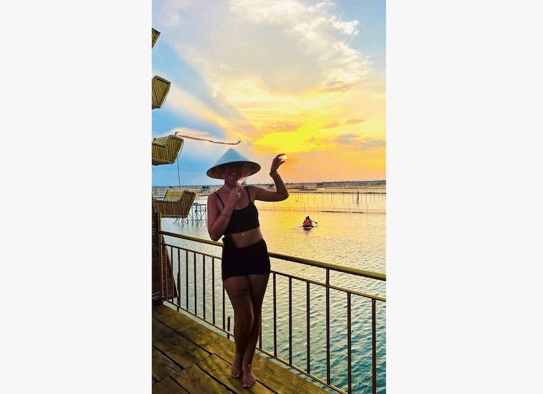 A person on a wooden deck overlooking a body of water with a sunset in the background. 1