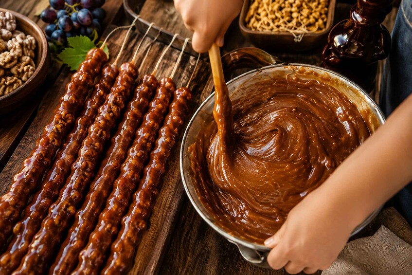 Skewers of meat being glazed with sauce, a bowl of sauce, and a bowl of nuts on a wooden surface. 1