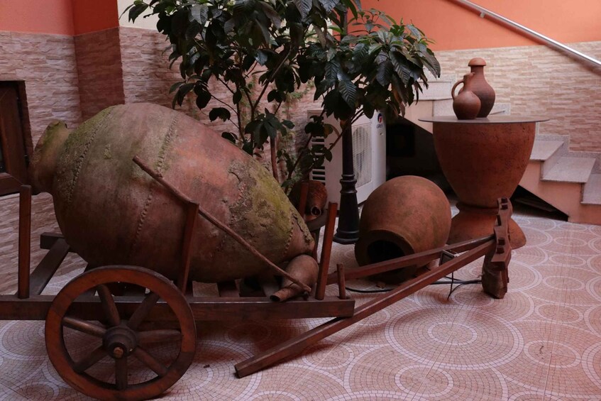 A rustic outdoor setting with a large, rusted wheelbarrow, a potted plant, and a traditional clay pot on a tiled floor. 5