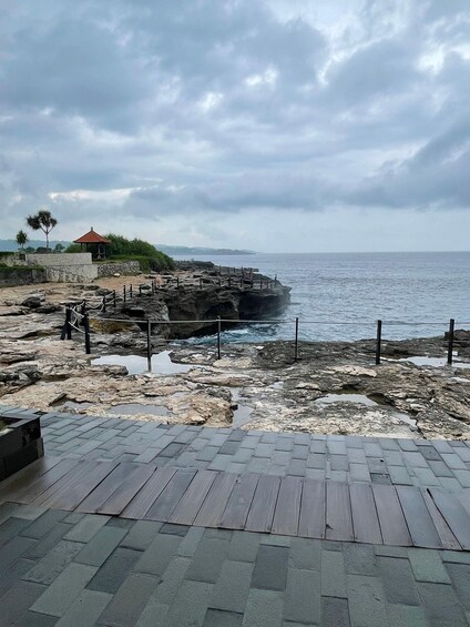 A rocky coastal area with a paved walkway, a small pavilion, and the sea in the background. 5