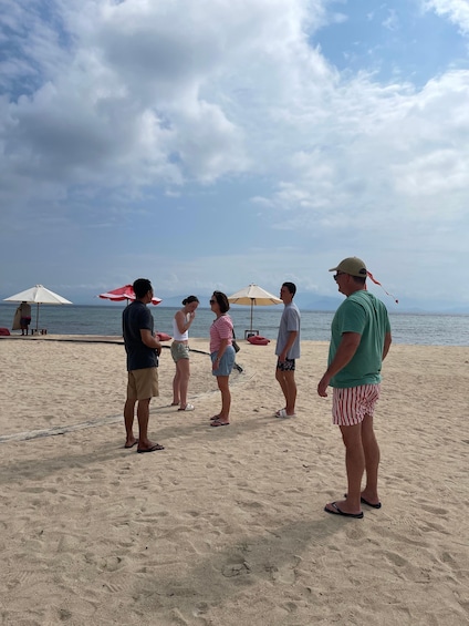 A group of people standing on a sandy beach with umbrellas and the ocean in the background. 3