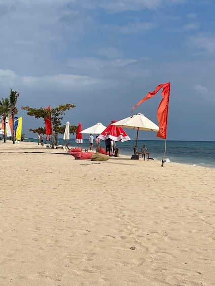 A beach with red and white umbrellas, palm trees, and a clear sky. 2