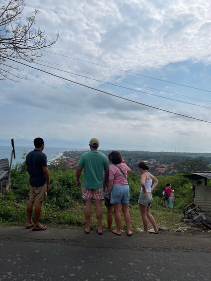 A group of people standing on a roadside overlooking a coastal landscape with houses and a distant view of the sea. 5