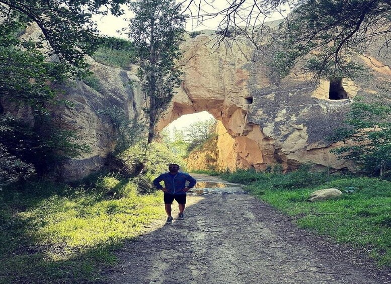 A person walking on a dirt path through a canyon with a large rock arch. 5