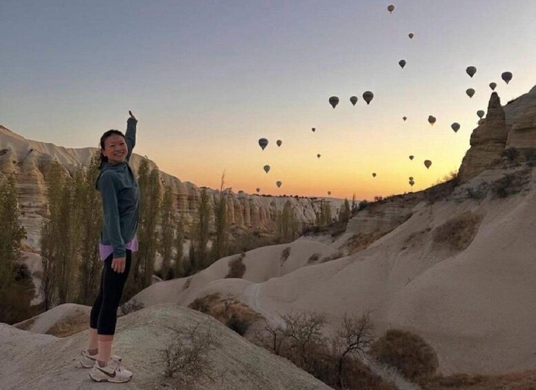 A person standing on a rock with a canyon in the background and hot air balloons in the sky. 4