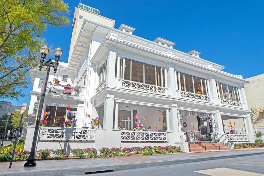 A white Victorian-style building with large windows, a balcony, and colorful flower arrangements. 3