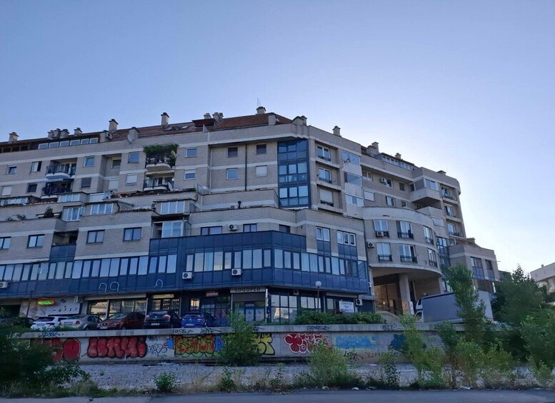 A multi-story building with balconies and a ground-level shop with graffiti. 1