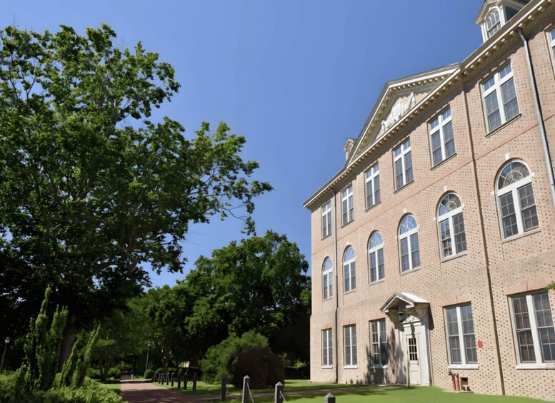 A large brick building with arched windows and a central entrance, surrounded by lush green trees and a clear blue sky. 4