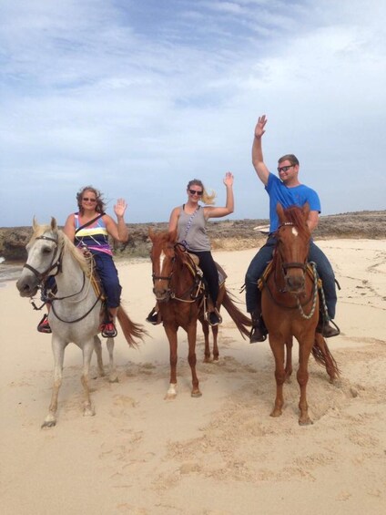 Three people riding horses on a sandy beach with a cloudy sky. 4