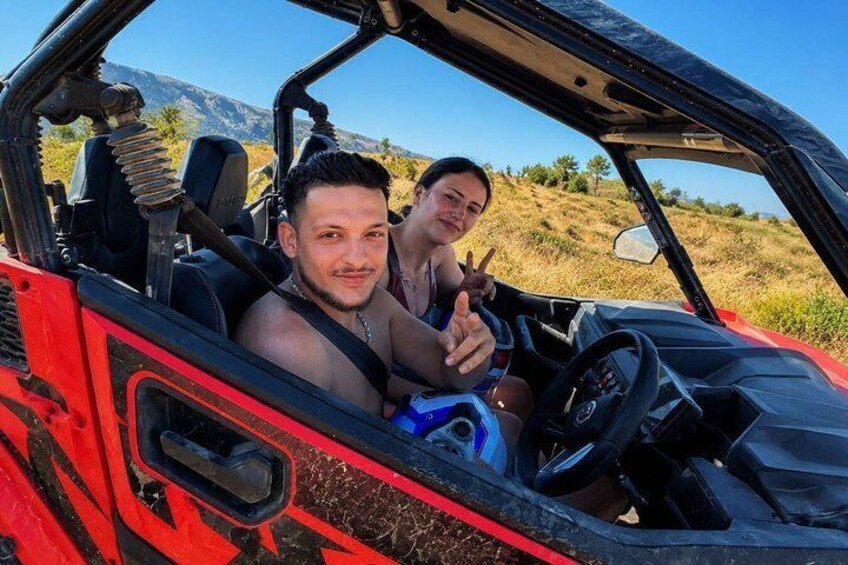 A red off-road vehicle with two people inside, a steering wheel, and a dashboard. 4
