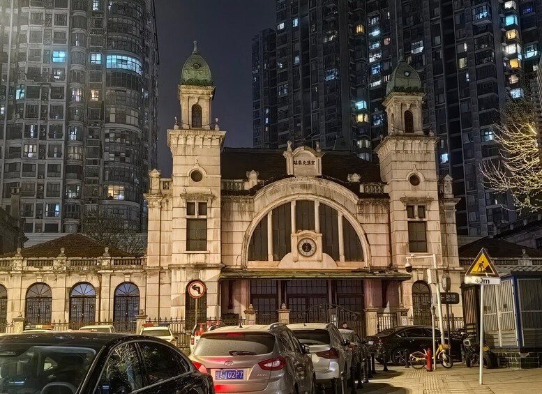 A historic building with a clock tower, surrounded by modern high-rise buildings at night. 4