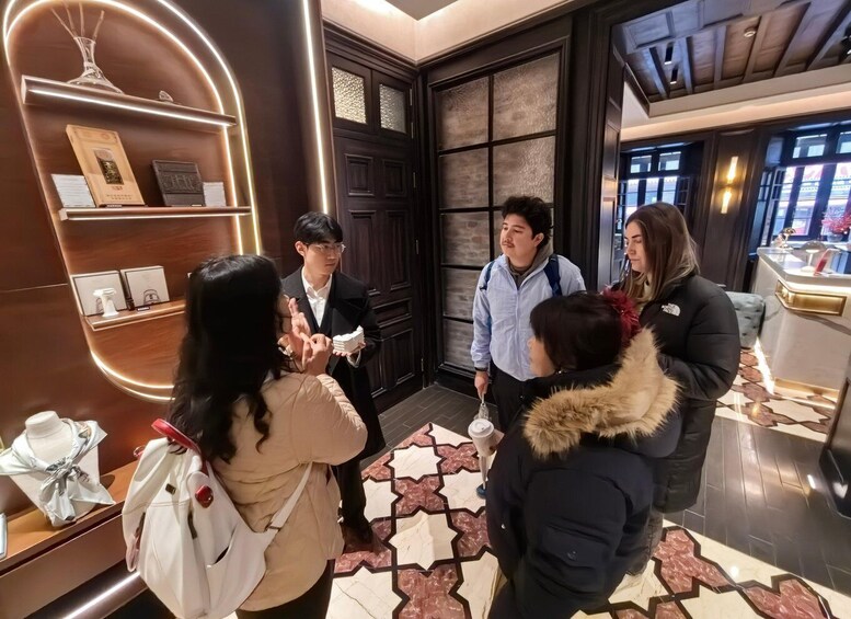 A group of people in a modern interior space with a wooden floor, a decorative wall with a circular light fixture, and a display of items on shelves. 1