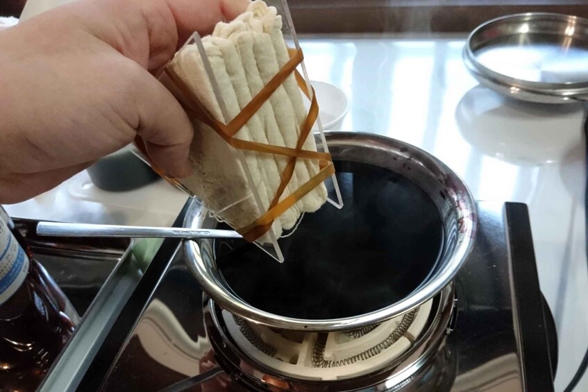 A hand holding a wrapped item over a pot on a stove. 5