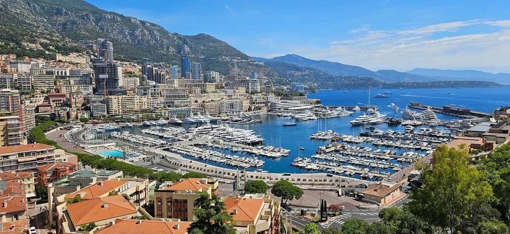 A coastal city with a marina filled with boats, surrounded by buildings and mountains. 1