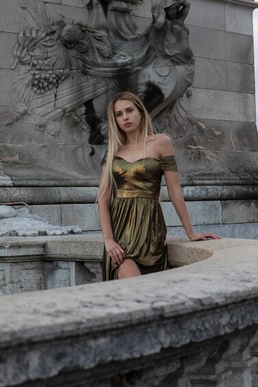 A person in a gold dress standing in front of a stone fountain with a detailed sculpture. 2
