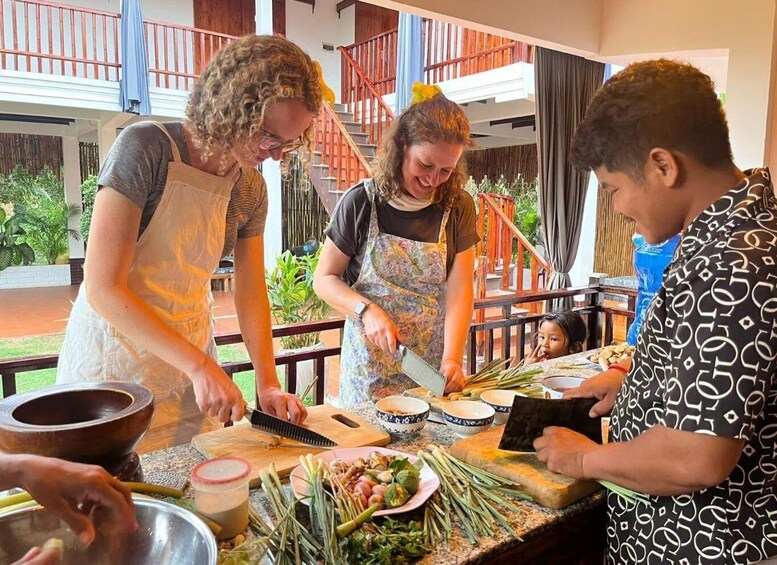 A group of people preparing food outdoors with a wooden table, plants, and a staircase in the background. 2