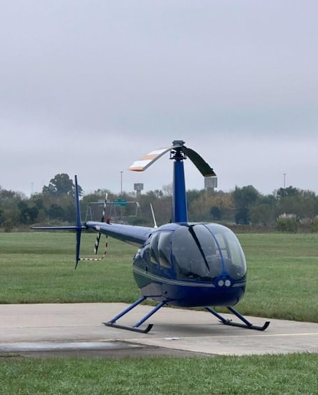 Sininen helikopteri betonipinnalla, taustalla ruohokenttä ja puita. 1