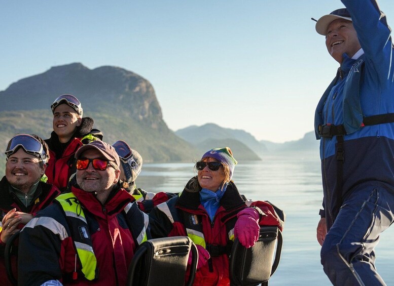 A group of people in winter gear on a boat with a mountainous landscape in the background. 5