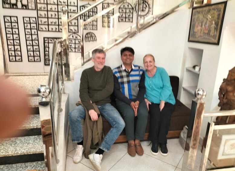 Three people sitting on a couch in a room with a staircase and framed pictures on the wall. 3