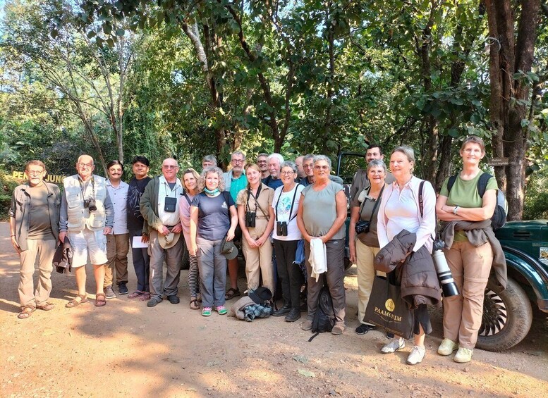 A group of people standing outdoors in a natural setting with trees and a dirt path. 2