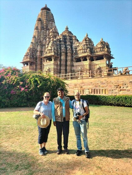 A temple with intricate carvings and a large spire, surrounded by greenery and a clear sky. 1