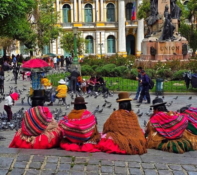 People in traditional attire sitting on the ground, pigeons, and a statue labeled 'UNION' in a public square. 1