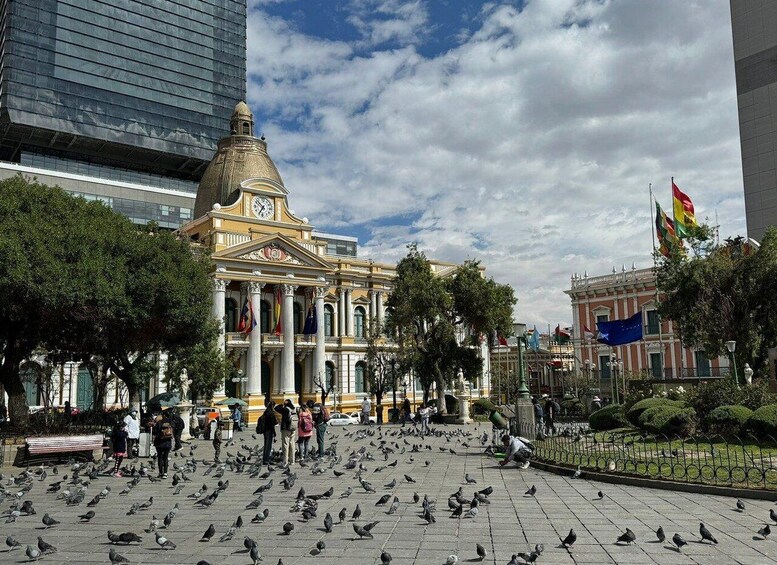 A plaza with pigeons, people, and historic buildings. 2