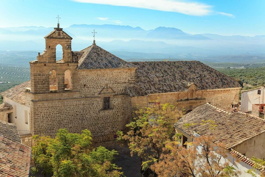 A historic stone church with a bell tower, surrounded by trees and a mountainous backdrop. 1