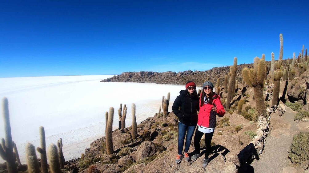 Two people standing on a rocky path with cacti and a salt flat in the background. 5
